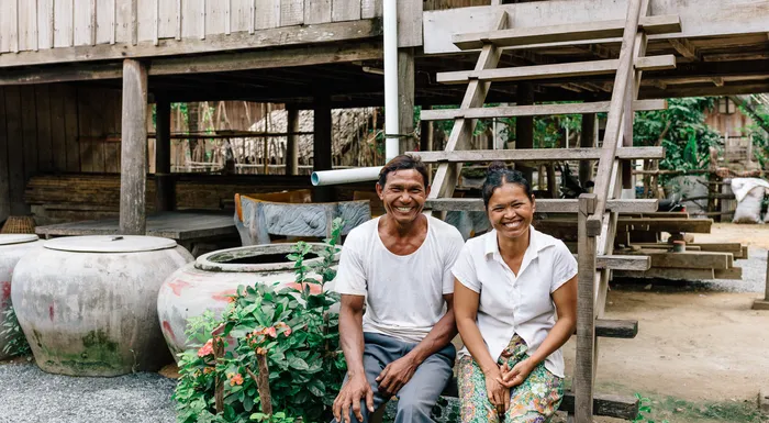 Young couple smiling while sitting on the steps outside of their home in Cambodia.