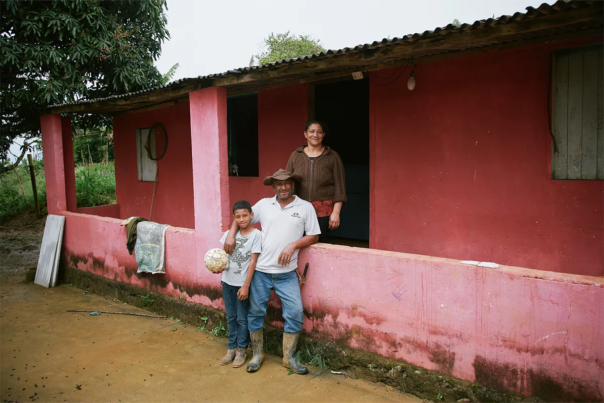 A young boy in Brazil smiles and holds a soccer ball while standing next to his parents.