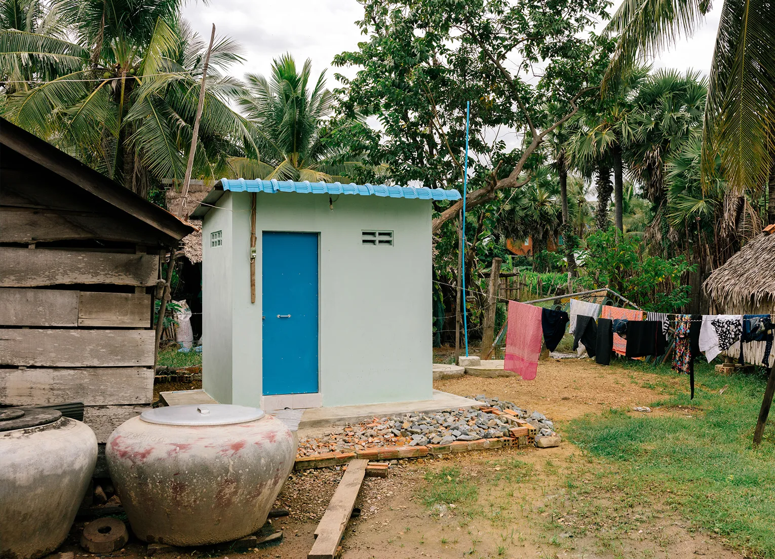 A blue outhouse next to a clothesline with hanging laundry.